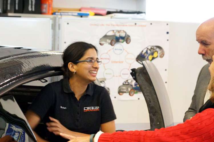 A female graduate student leans out of a car in a CUICAR lab while talking to two visitors