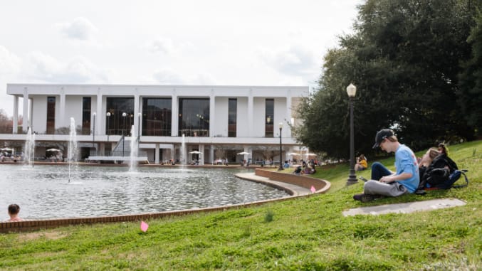 Clemson undergraduate students study in a grassy spot beside the reflection pond and Cooper Library.