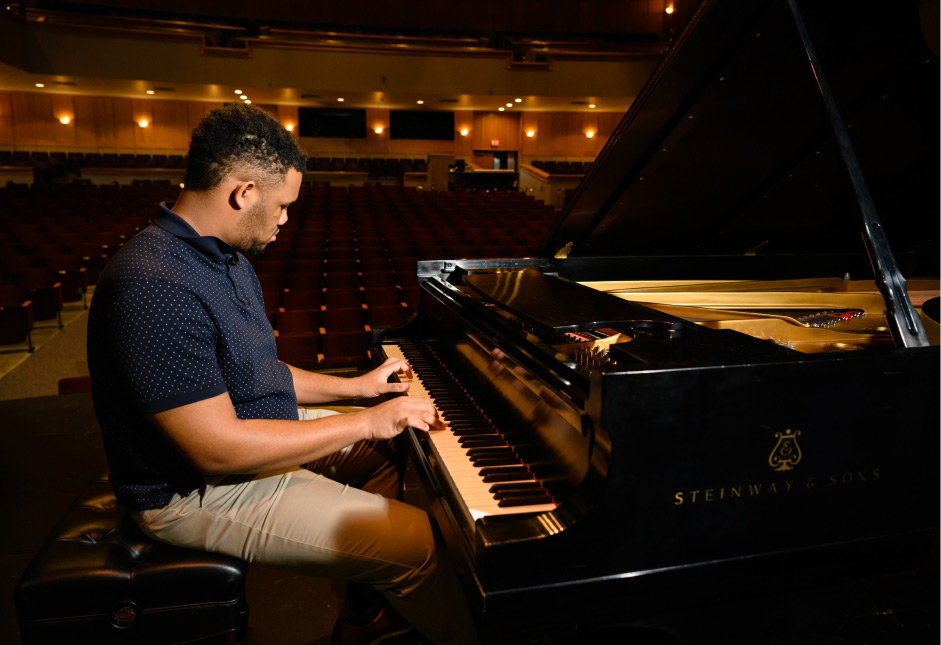 A male student sits at a piano on stage at the Brooks performing arts center