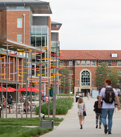 People walk on the sidewalk beside McAlister Hall and the Quad.