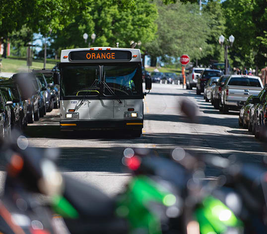 A cat bus drives down a tree-lined street on campus.