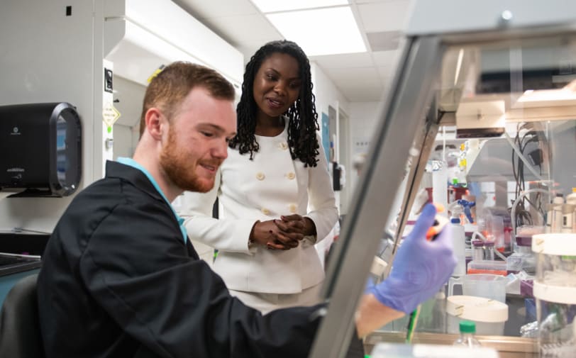 Female faculty member watches as her student conducts an experiment in the lab.