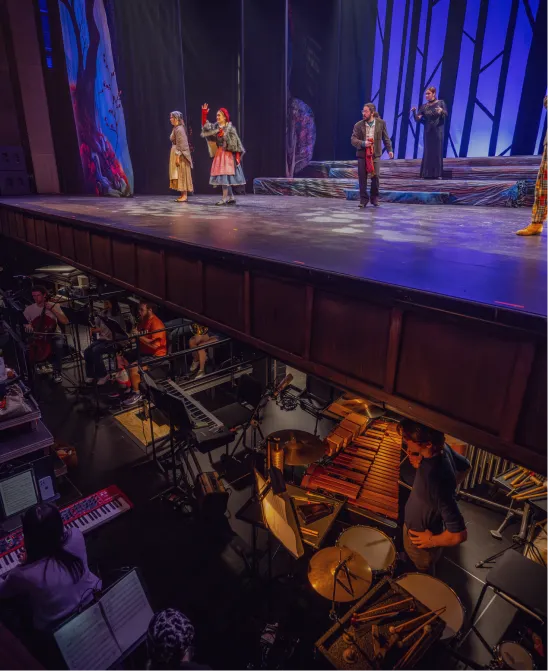 A full orchestra pit beneath a stage is visible during a theatrical performance on stage at the Brooks Center for the Performing Arts.