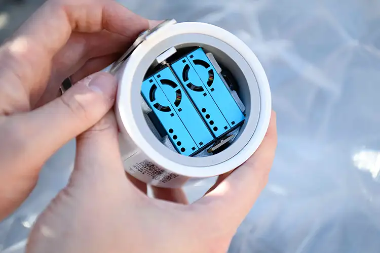 A pair of hands holding an open cylindrical sensor, revealing two blue electronic modules inside.