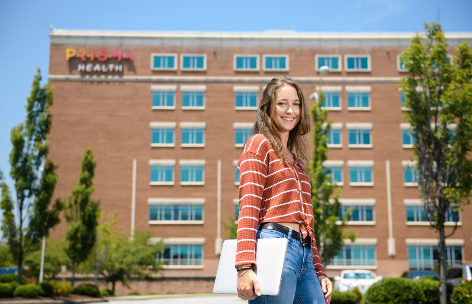 A female student with a notepad stands outside a prisma health hospital