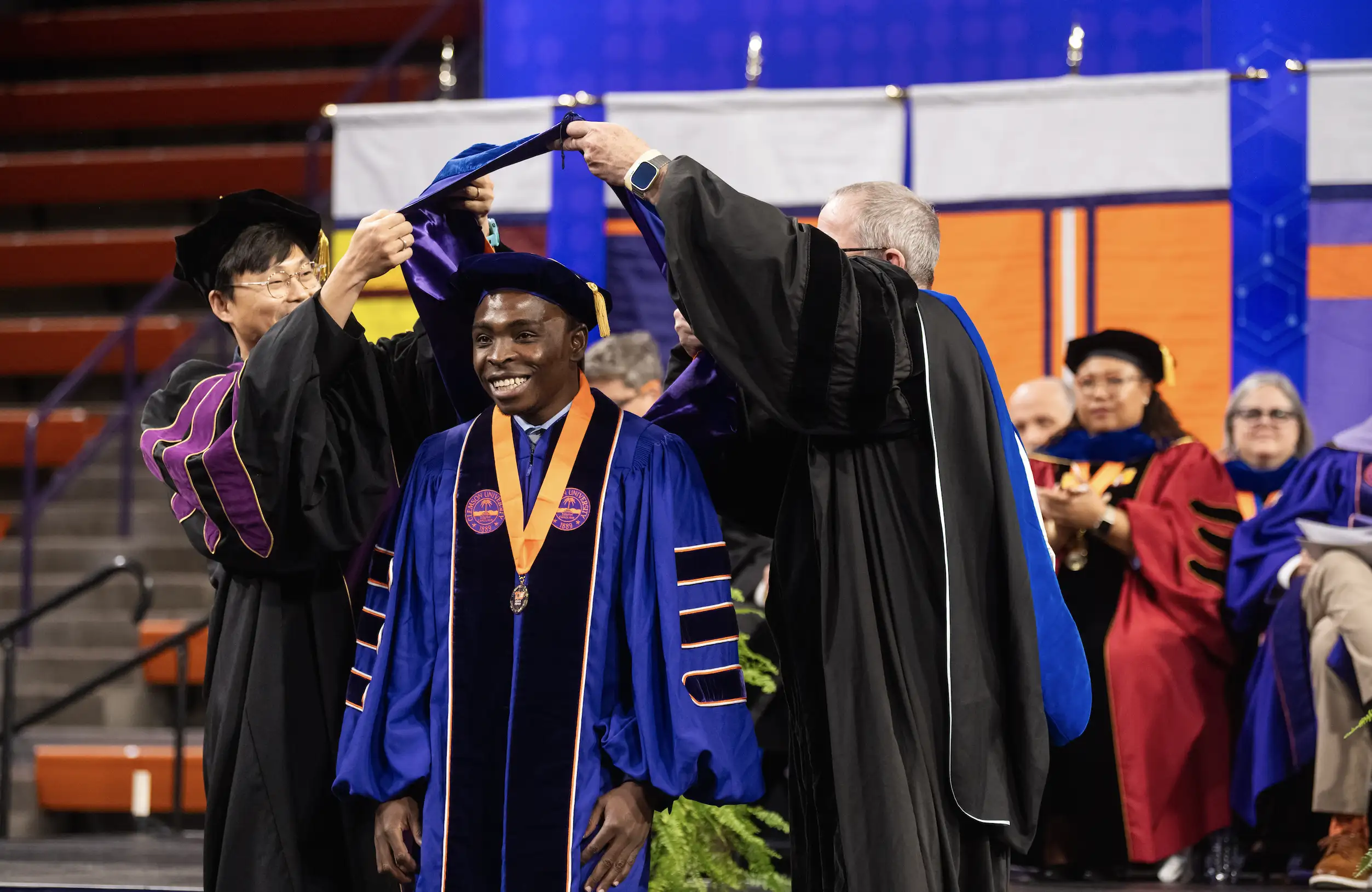A graduating Clemson student receives his doctoral hood from two Clemson faculty members.