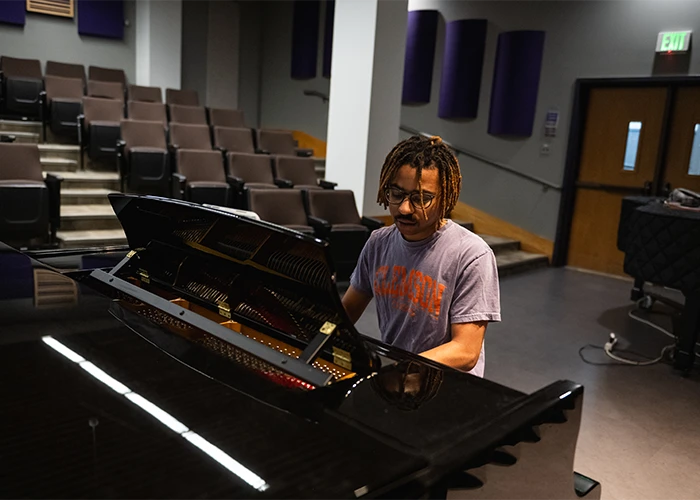 A male student in a Clemson t-shirt practices piano in a small, empty auditorium.