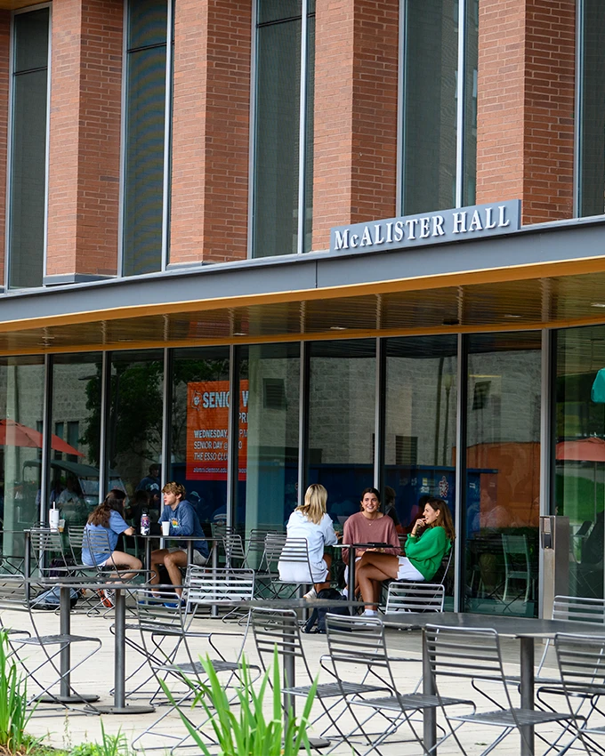 students sit together at tables outside in front of the large glass windows of McCalister dining hall