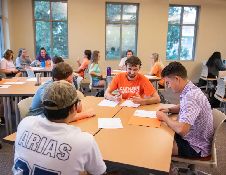 A female student wears a gray sweater and denim jeans next to an open barn door.