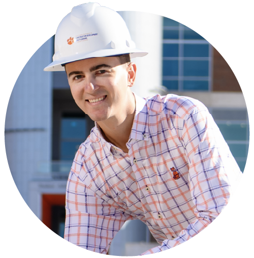A male student wearing khaki pants, an orange-and-purple checkered button-down shirt and a white construction hard hat.