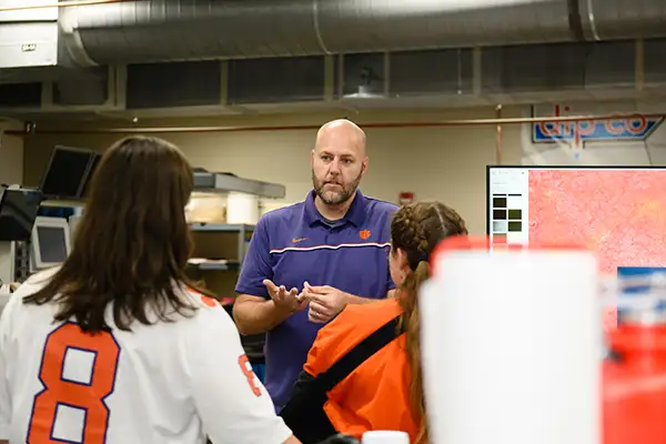 A man in a purple shirt engages in conversation with a group of people on a department tour.