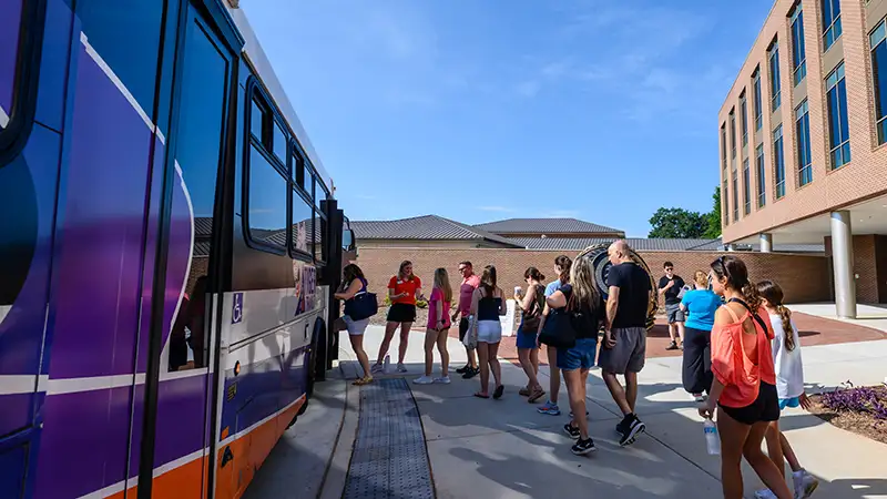 A group of adults and high school students board a bus at the Nieri Family Alumni and Visitors Center for a campus tour.