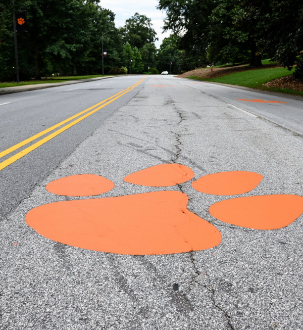 An orange Clemson Tiger Paw is spray painted on an asphalt road.