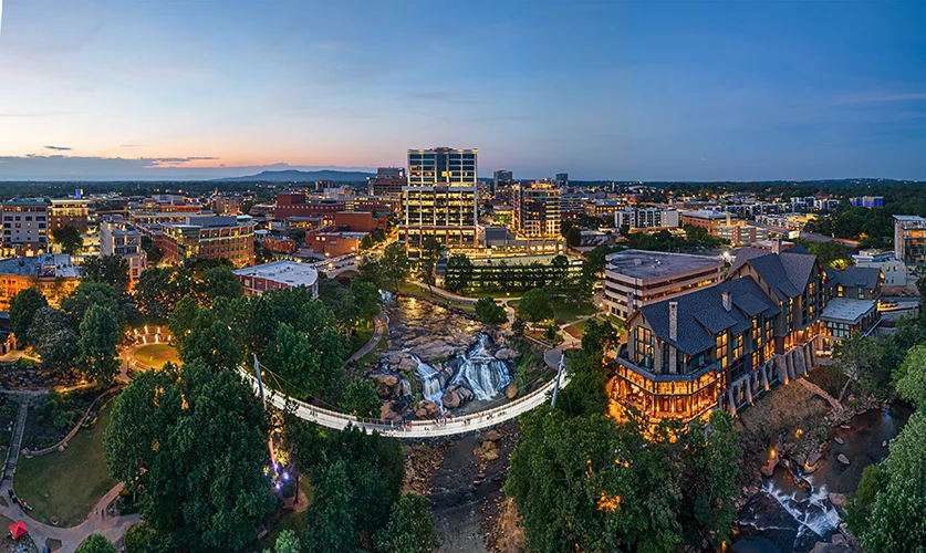 An aerial view of downtown greenville with a large bridge and waterfall in the foreground and city streets in the background