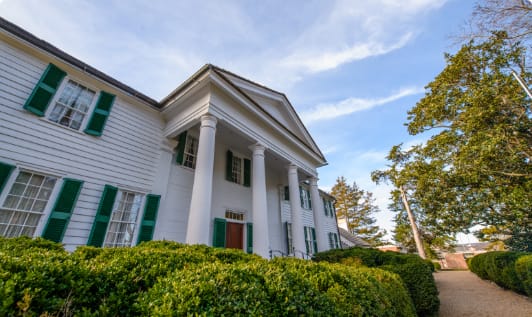 A white house with four pillar columns in the front and green shutters.