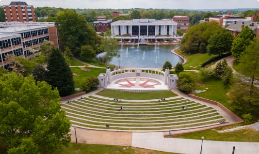 An outdoor amphitheater and its seating in the foreground with a fountain reflection pond and R.M. Cooper Library in the background.