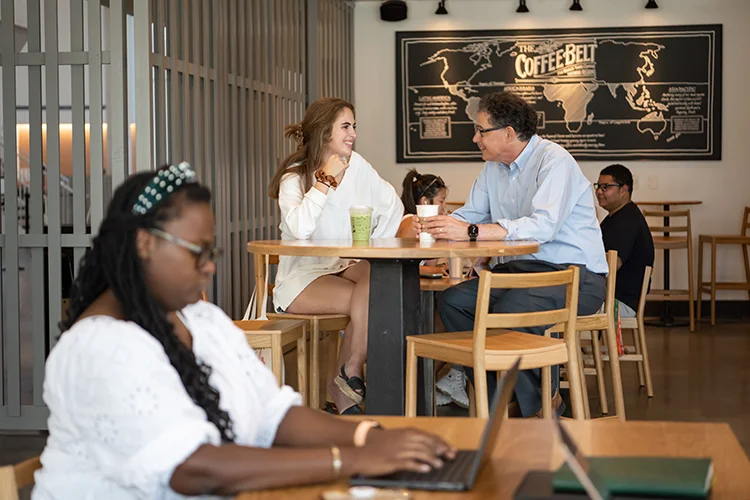 A male professor and female student sit together at a high-top table in a coffee shop.